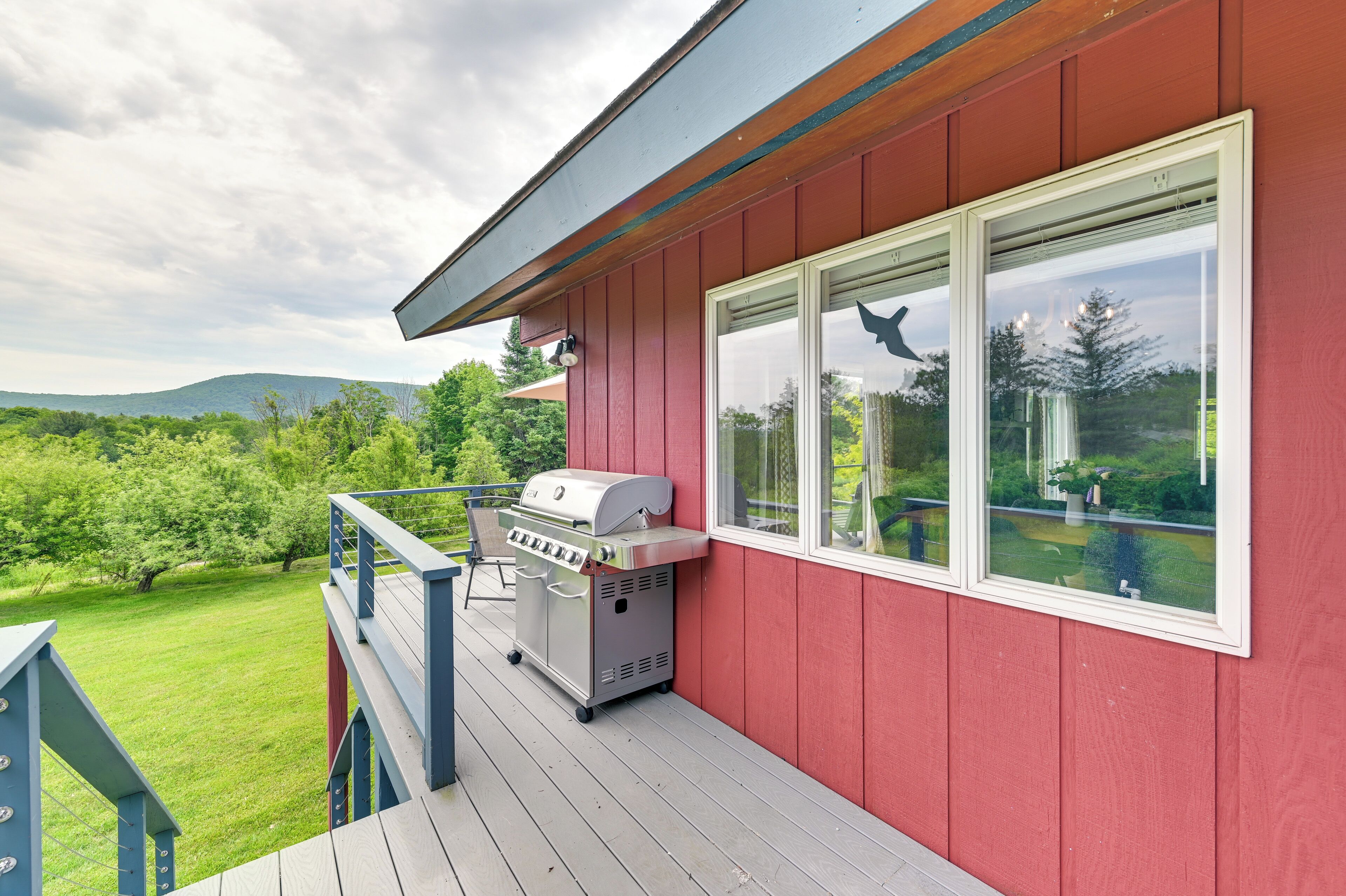A red building with a deck, a barbecue grill, and a view of a green landscape.