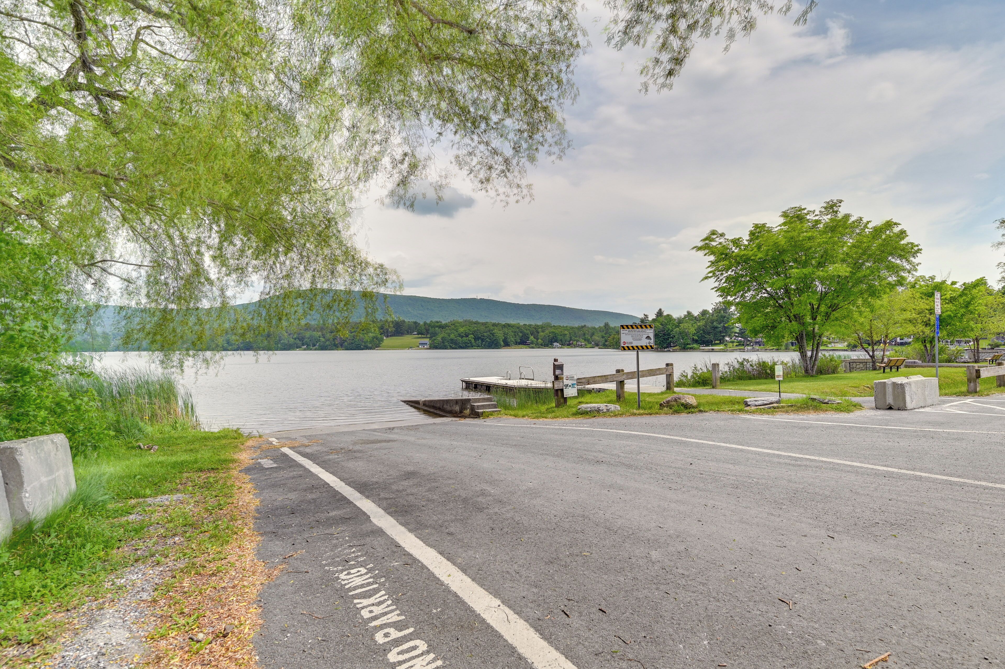 A paved road with a pedestrian crossing, a dock, and a body of water with trees and hills in the background.