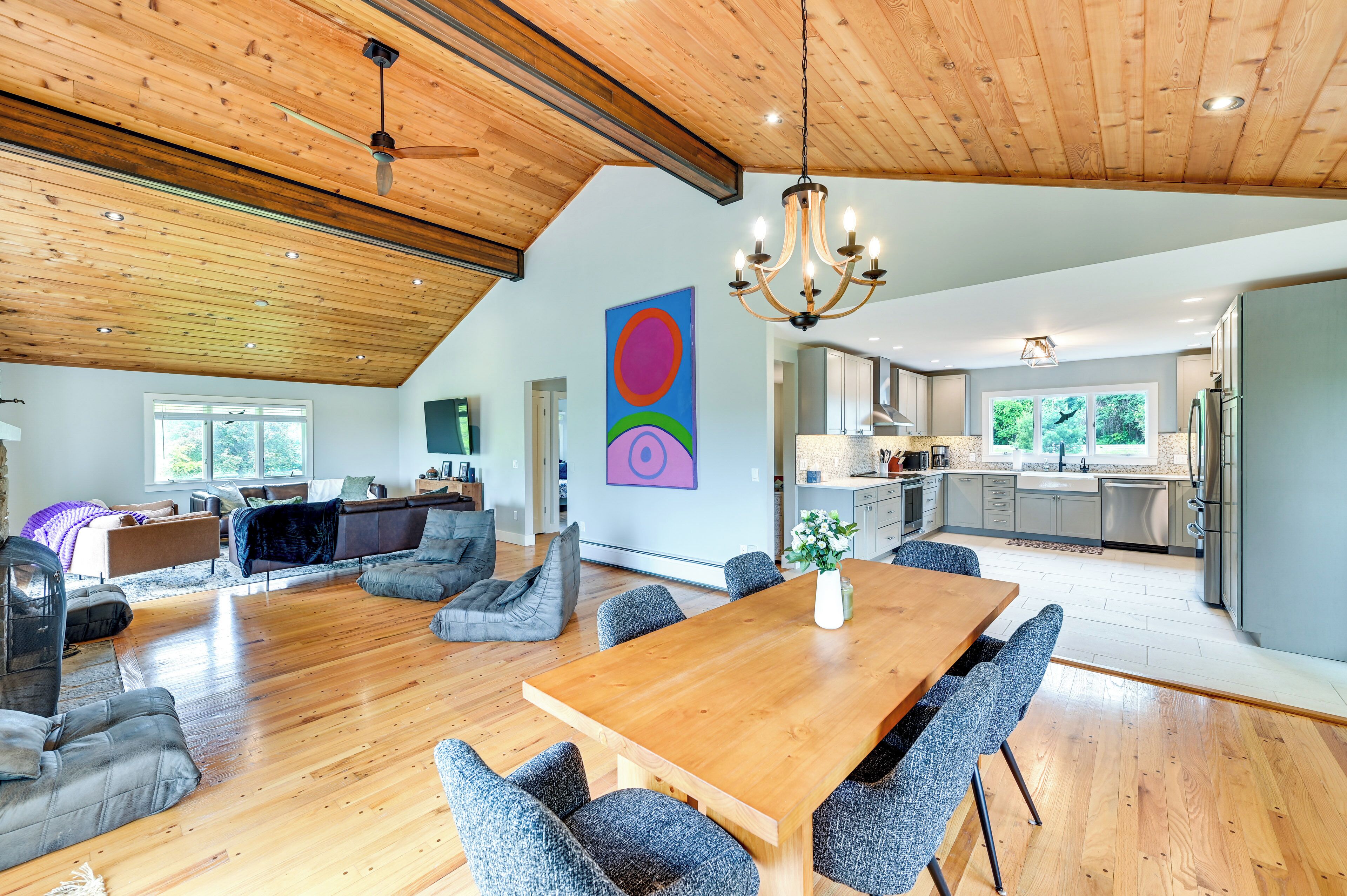 A spacious living area with a wooden ceiling, a dining table, and grey upholstered seating.