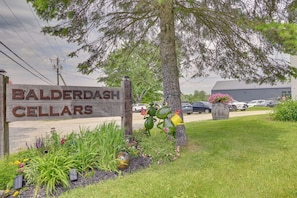 A sign for Balderdash Cellars with a wooden fence, a tree, and a parking lot in the background.