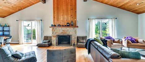 A spacious living area with a stone fireplace, wooden ceiling, and large windows.