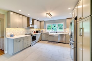 A modern kitchen with light grey cabinets, stainless steel appliances, and a large window providing a view of greenery.