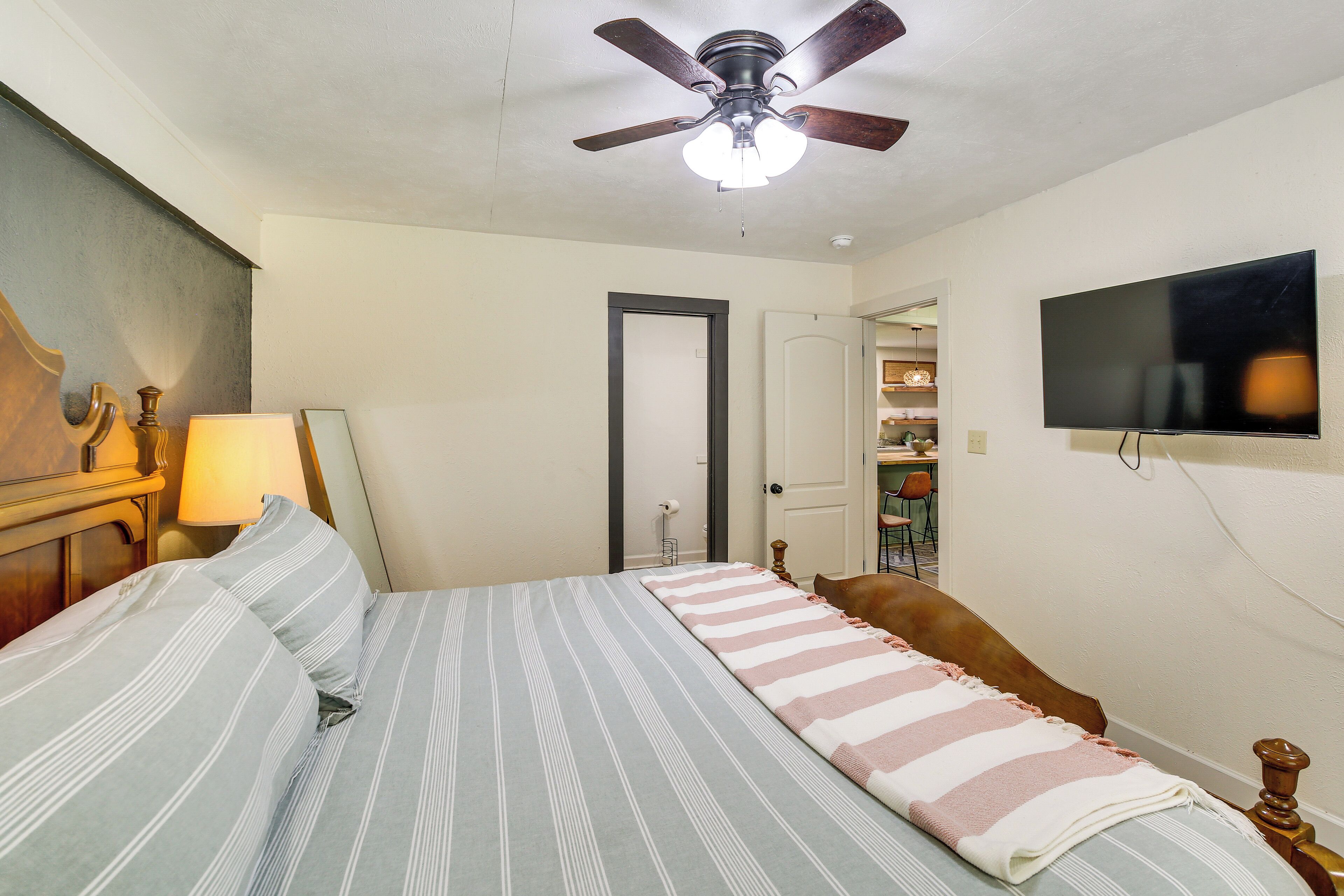 A bedroom with a bed, a ceiling fan, a TV, and a door leading to another room.