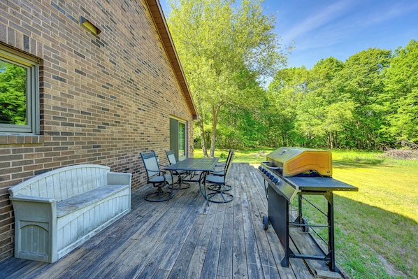 A patio with a wooden table and chairs, a built-in bench, and a barbecue grill.