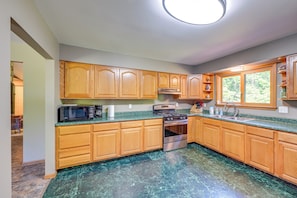 A kitchen with wooden cabinets, a stainless steel stove, a microwave, and a window with a view of greenery. - Wooded Applegate Retreat w/ Private Trail Access (Carsonville)