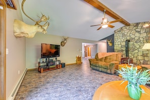 A living room with a stone wall, mounted deer heads, a ceiling fan, a fireplace, a television, and a plush sofa.