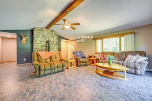 A spacious living room with a stone accent wall, a ceiling fan, and a large window with curtains.