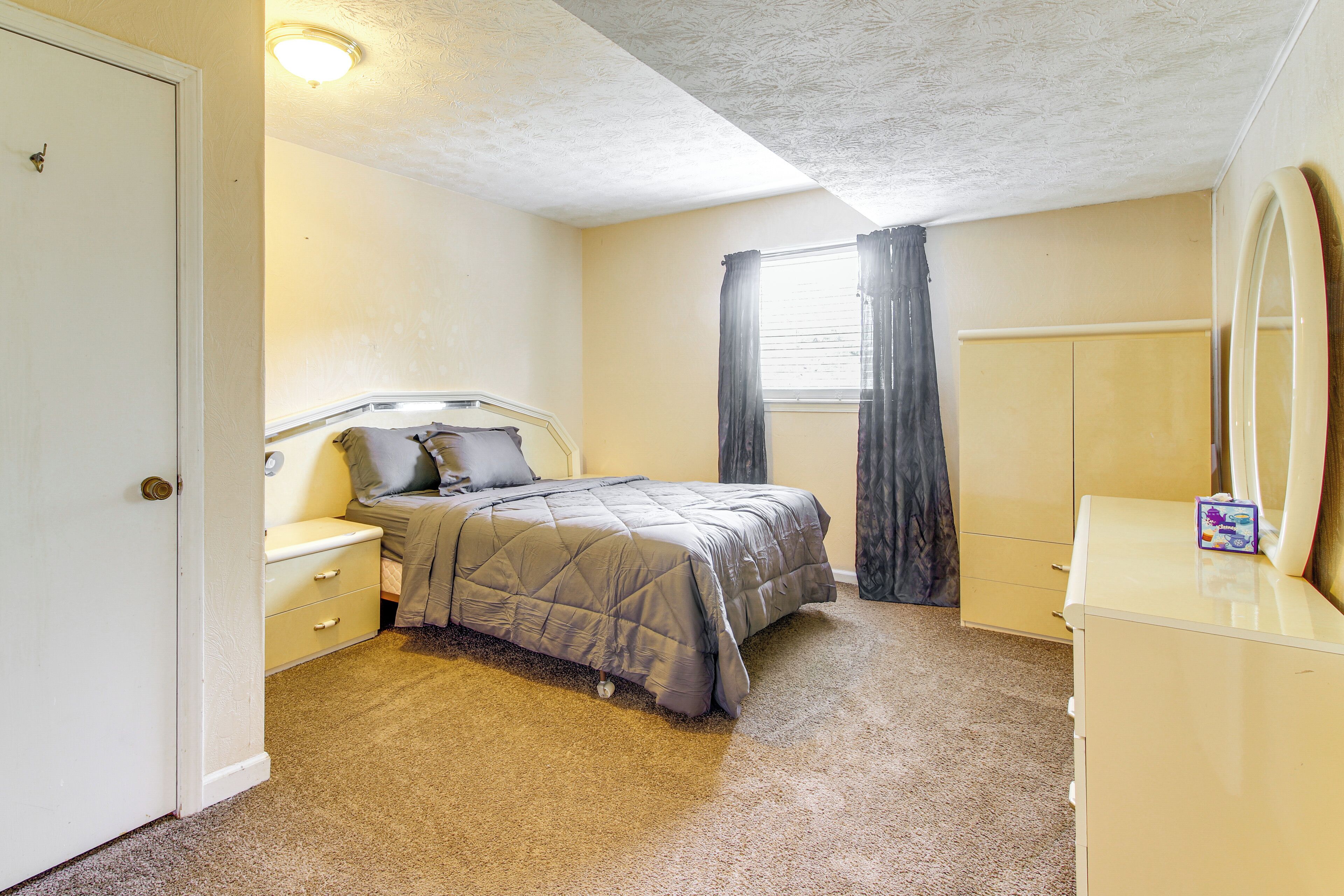 A bedroom with a bed, nightstand, dresser, and a window with curtains.