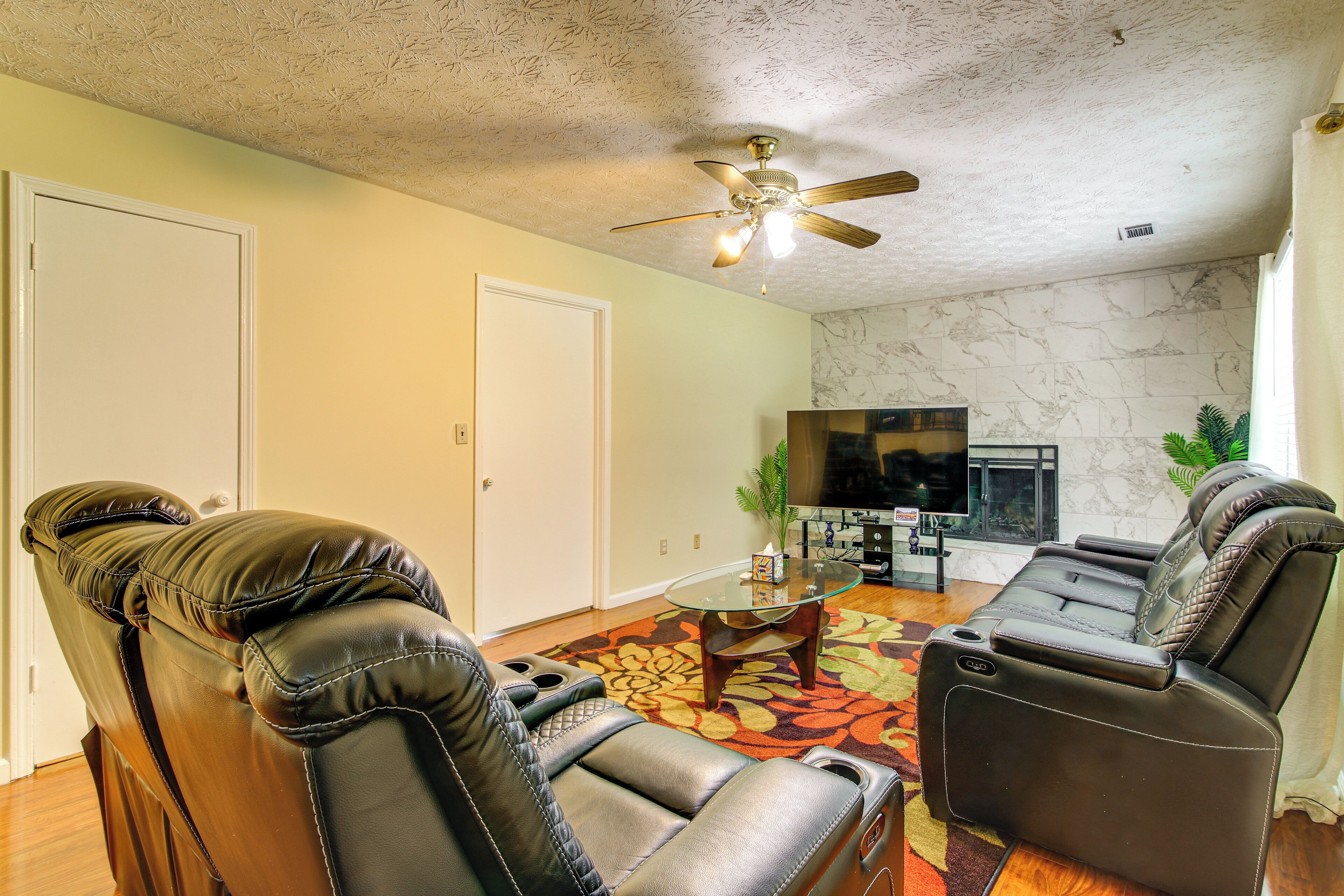 A living room with a ceiling fan, a glass coffee table, and a fireplace.