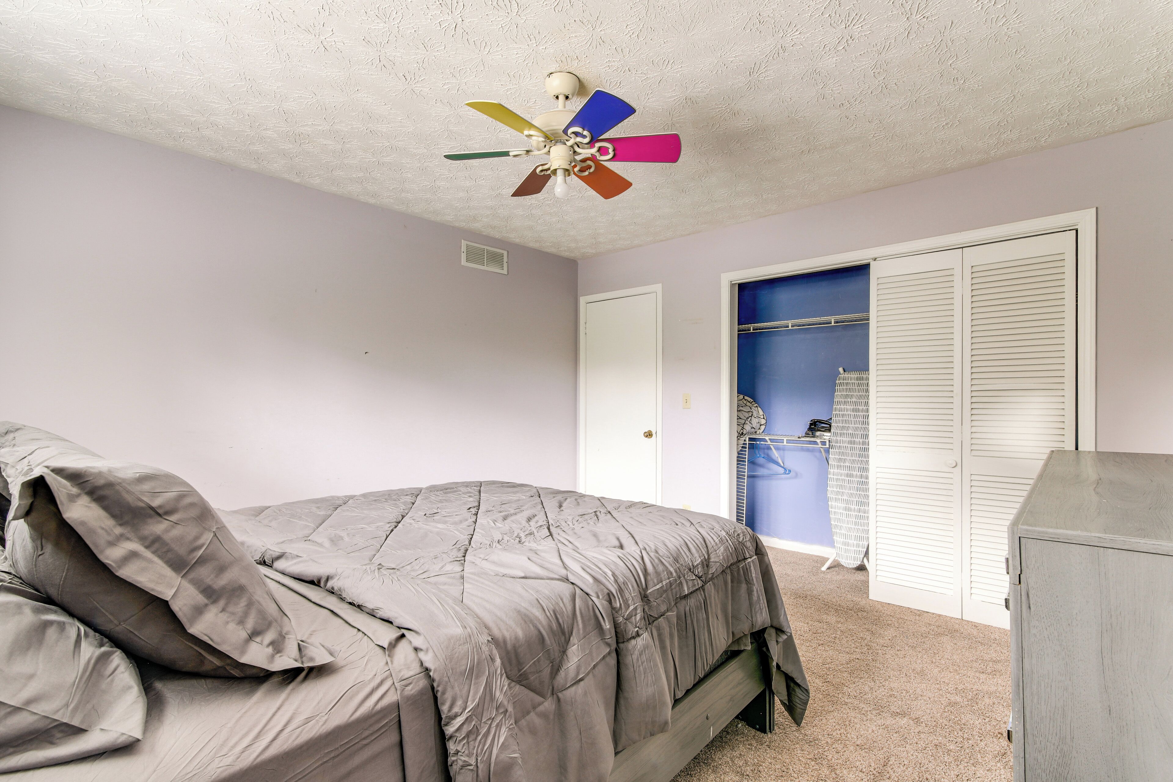 Un dormitorio con cama, ventilador de techo, armario y vestidor con interior azul.