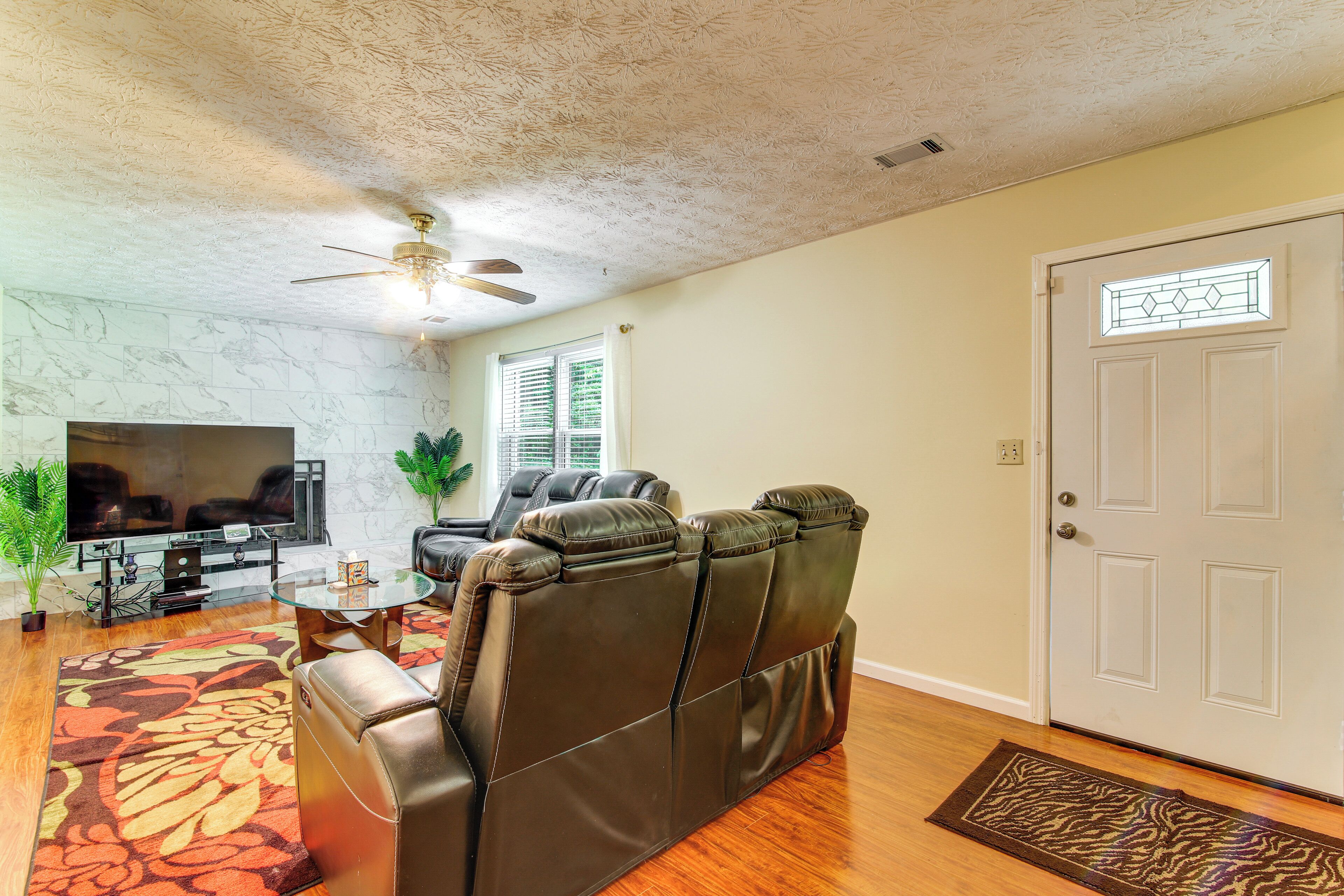 A living room with a leather sofa, a flat-screen TV, a ceiling fan, and a door with a window.