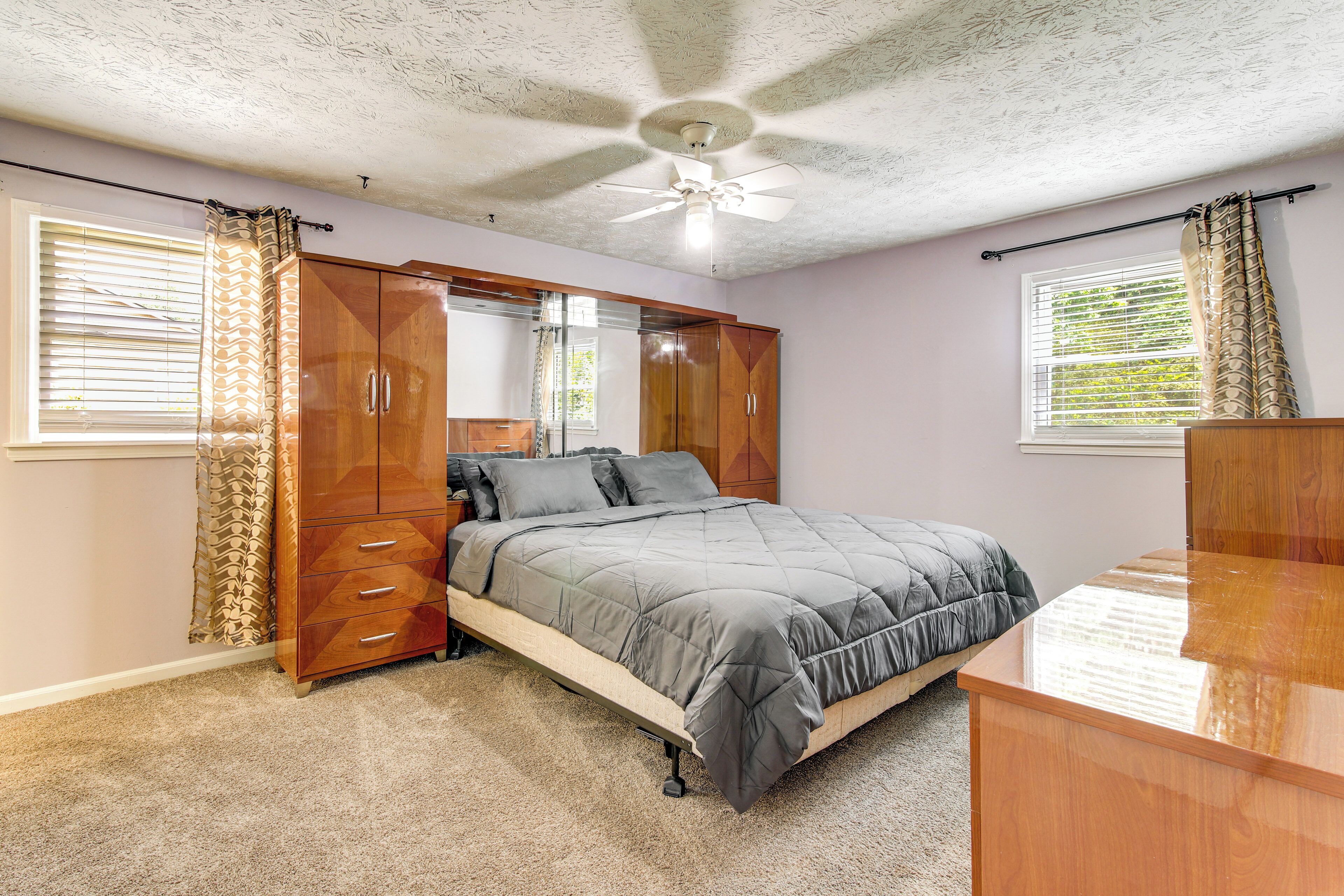 Un dormitorio con cama, armario, ventilador de techo y ventanas con cortinas.