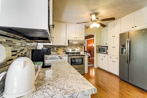 A kitchen with white cabinets, a stainless steel refrigerator, a microwave, a stove, and a ceiling fan. - 7 Mi to Stone Mtn Park! Spacious Family Getaway (Lilburn)