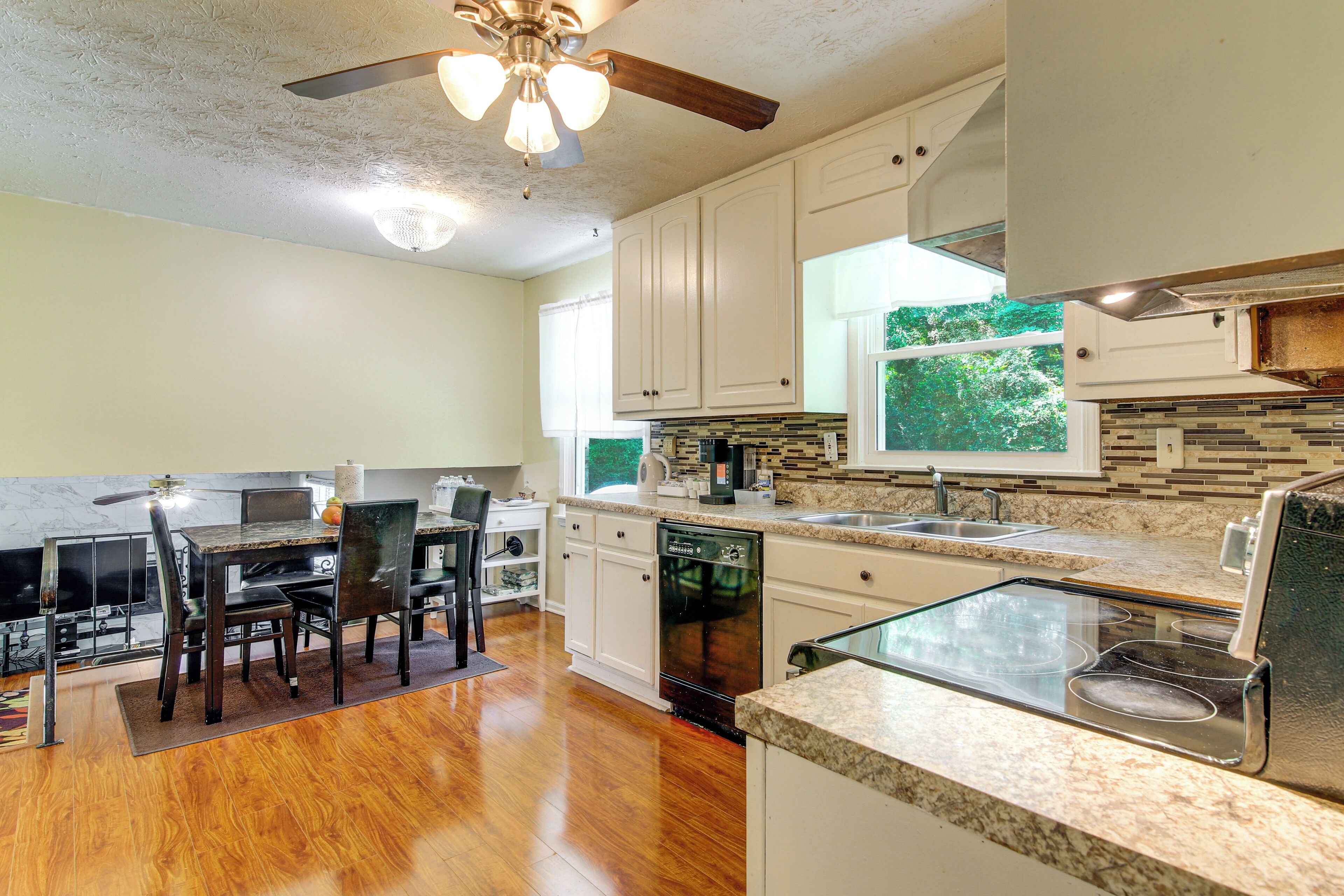 A kitchen with white cabinets, a dishwasher, a stove, and a dining area with chairs and a table.