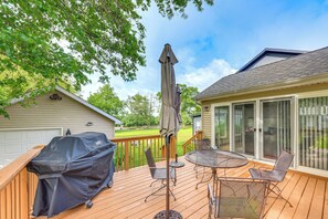 A wooden deck with a covered grill, outdoor table and chairs, and a large umbrella.