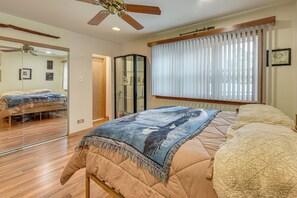 A bedroom with a bed, a ceiling fan, a window with blinds, and a mirror.