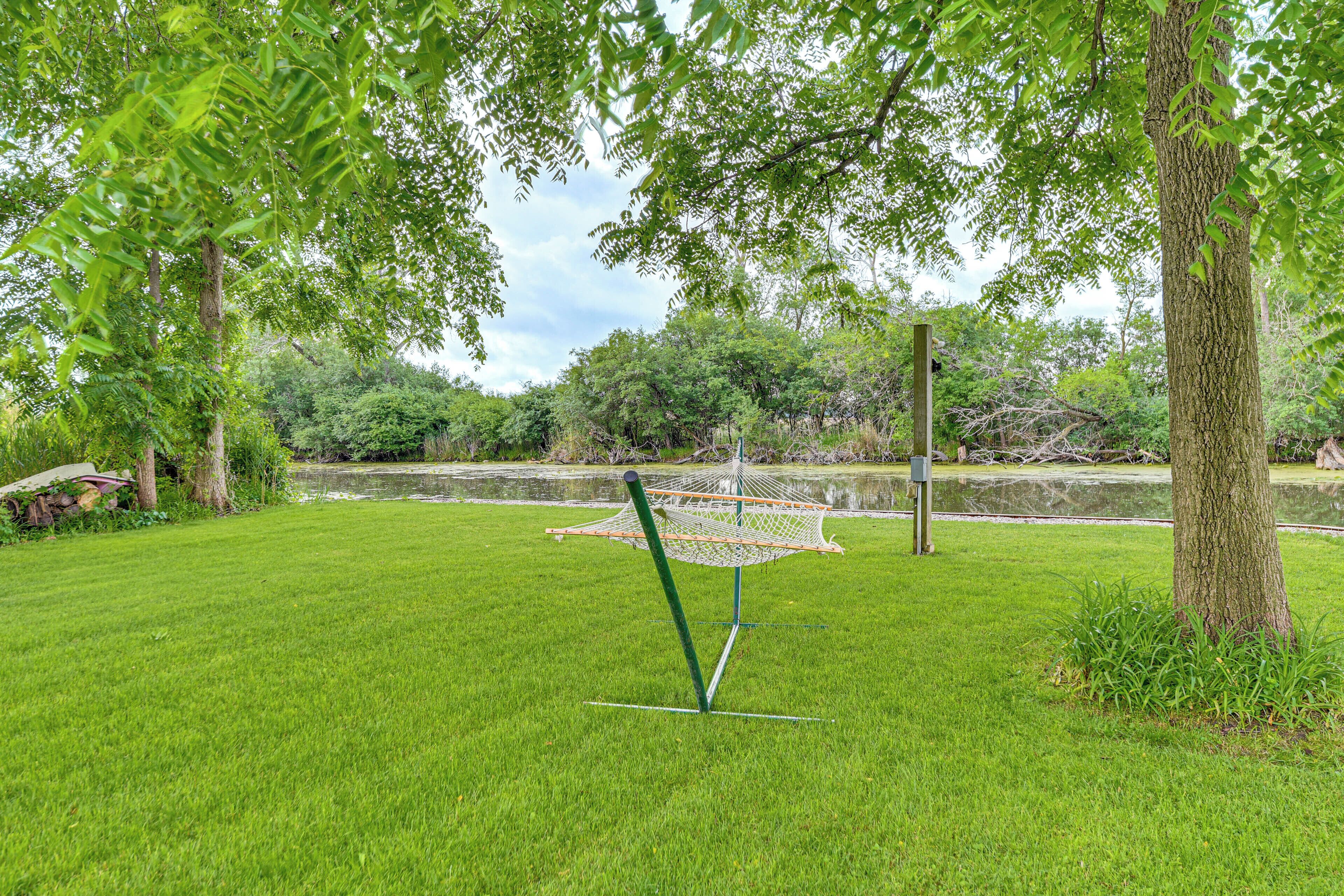 A grassy area with a hammock, trees, and a pond.