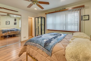 A bedroom with a bed, a ceiling fan, a window with blinds, and a mirror.