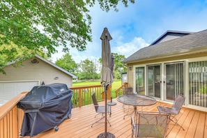A wooden deck with a covered grill, outdoor table and chairs, and a large umbrella.