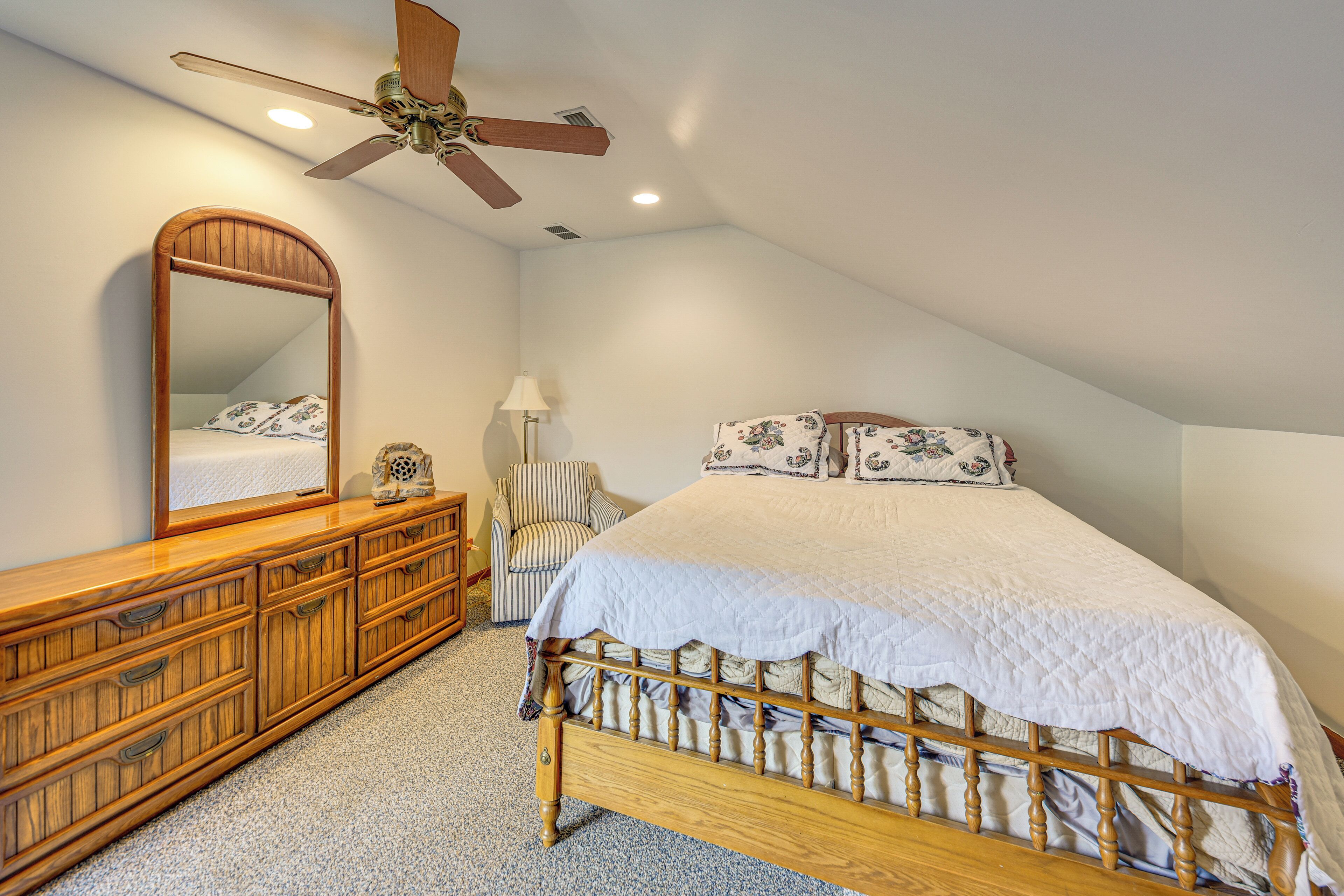 A bedroom with a wooden bed, a large mirror, a ceiling fan, and a chair.