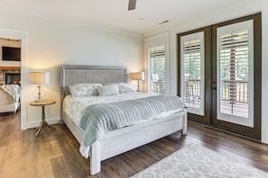 A bedroom with a bed, two bedside tables, a lamp, a fireplace, and a view through a door with blinds.