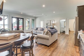 A spacious living area with a sofa, dining table, and chairs, a kitchen with a refrigerator, and large windows offering a view.