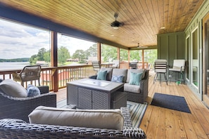 A covered outdoor deck with wicker furniture, a table, and a view of a lake.