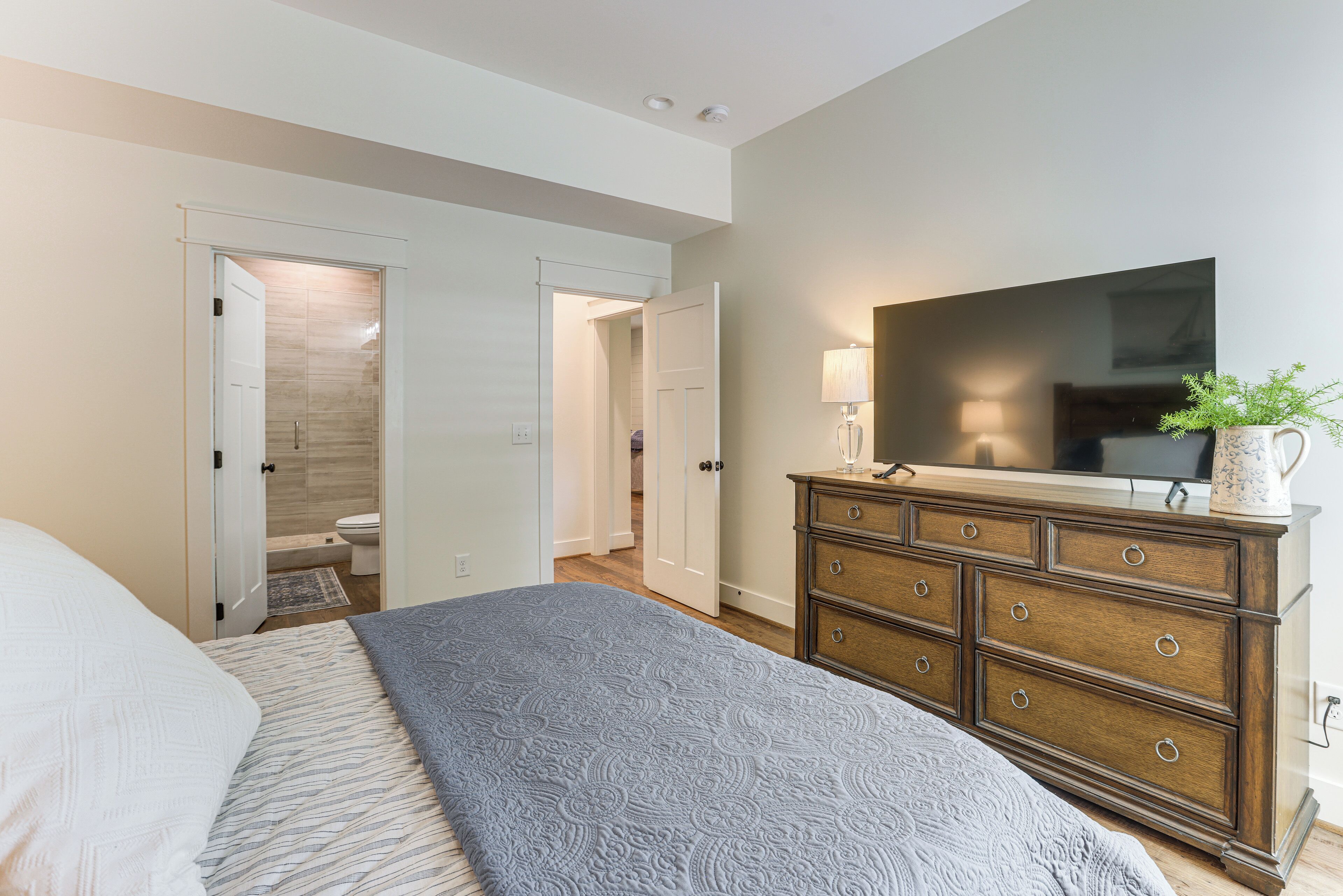 Een slaapkamer met een bed, een dressoir, een televisie en een badkamer zichtbaar door een geopende deur.