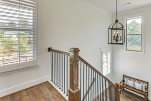 A staircase with wooden balusters and a metal handrail, a bench with a cushion, and a hanging light fixture.
