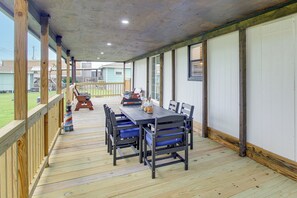 A covered outdoor dining area with a wooden deck, a table with chairs, and a view of a grassy yard.