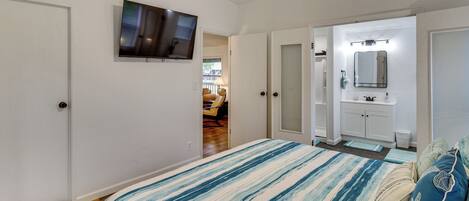 A bedroom with a bed, a TV mounted on the wall, and a door leading to a bathroom.
