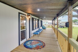 A covered porch with a row of blue chairs, a wooden deck, and a decorative rug.