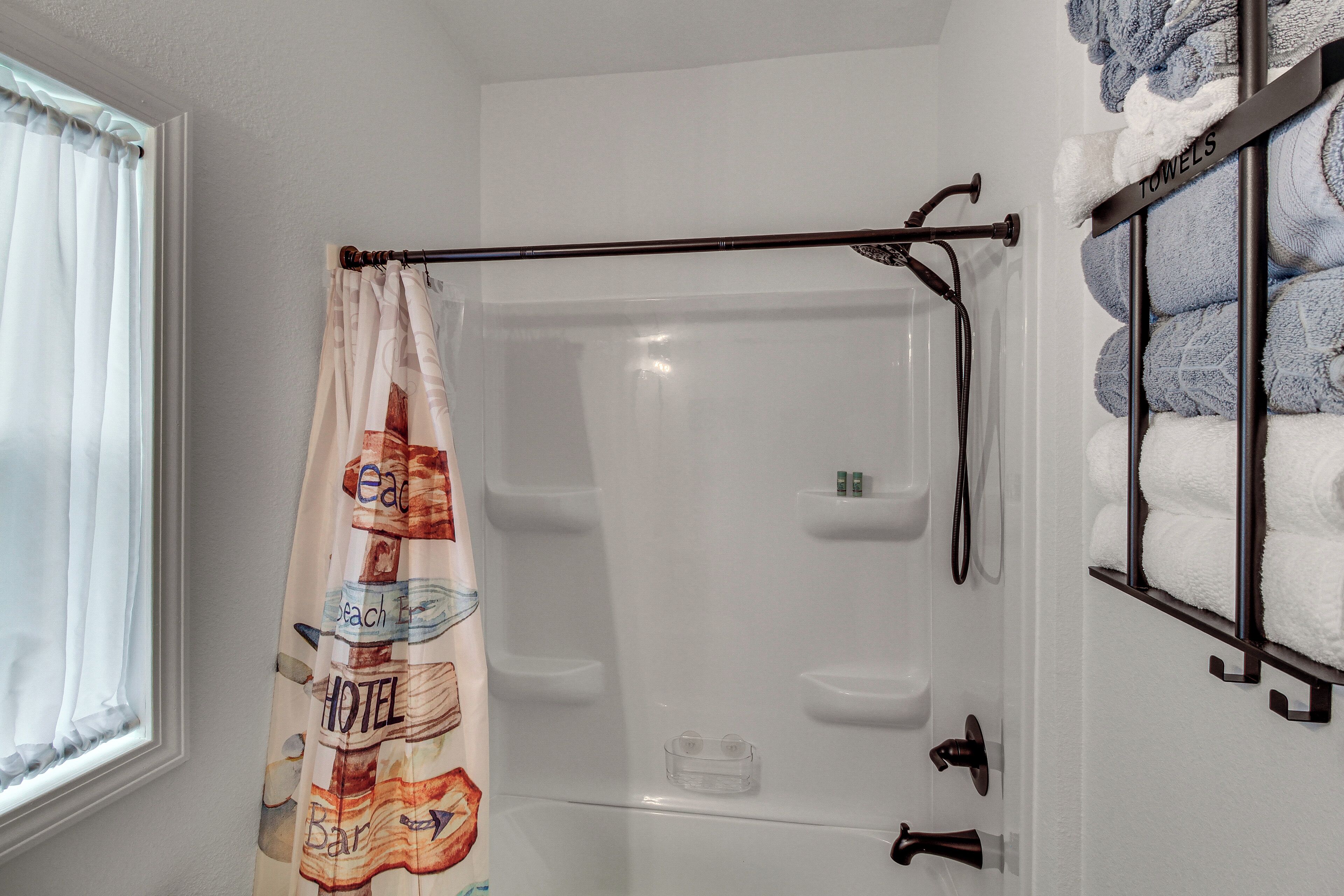 Une salle de bain avec un rideau de douche, un porte-serviettes avec des serviettes et une fenêtre avec un rideau.