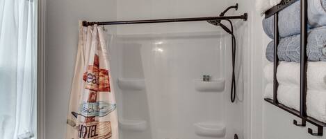 Une salle de bain avec un rideau de douche, un porte-serviettes avec des serviettes et une fenêtre avec un rideau.
