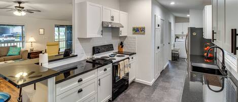 A modern kitchen with white cabinets, a black countertop, and a stainless steel range hood.