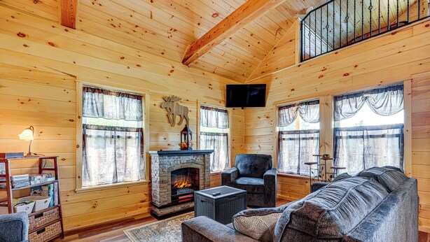 A log cabin interior with a fireplace, a sofa, a chair, and a television. - Hike, Hunt & Golf! Cabin on 4 Acres in Naples (Naples)