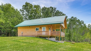 A log cabin with a porch, surrounded by a grassy area and trees. - Hike, Hunt & Golf! Cabin on 4 Acres in Naples (Naples)