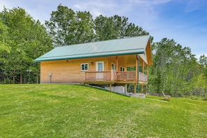 A log cabin with a porch, surrounded by a grassy area and trees. - Hike, Hunt & Golf! Cabin on 4 Acres in Naples (Naples)