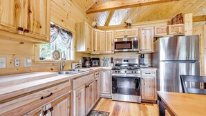 A wooden cabin-style kitchen with wooden cabinets, a stainless steel refrigerator, a stove, and a microwave. - Hike, Hunt & Golf! Cabin on 4 Acres in Naples (Naples)