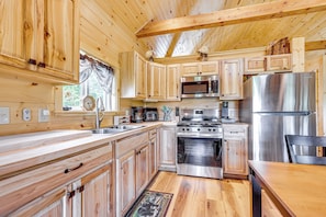 A wooden cabin-style kitchen with wooden cabinets, a stainless steel refrigerator, a stove, and a microwave. - Hike, Hunt & Golf! Cabin on 4 Acres in Naples (Naples)