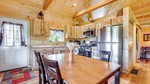 A wooden cabin interior with a kitchen, dining area, and a large window. - Hike, Hunt & Golf! Cabin on 4 Acres in Naples (Naples)