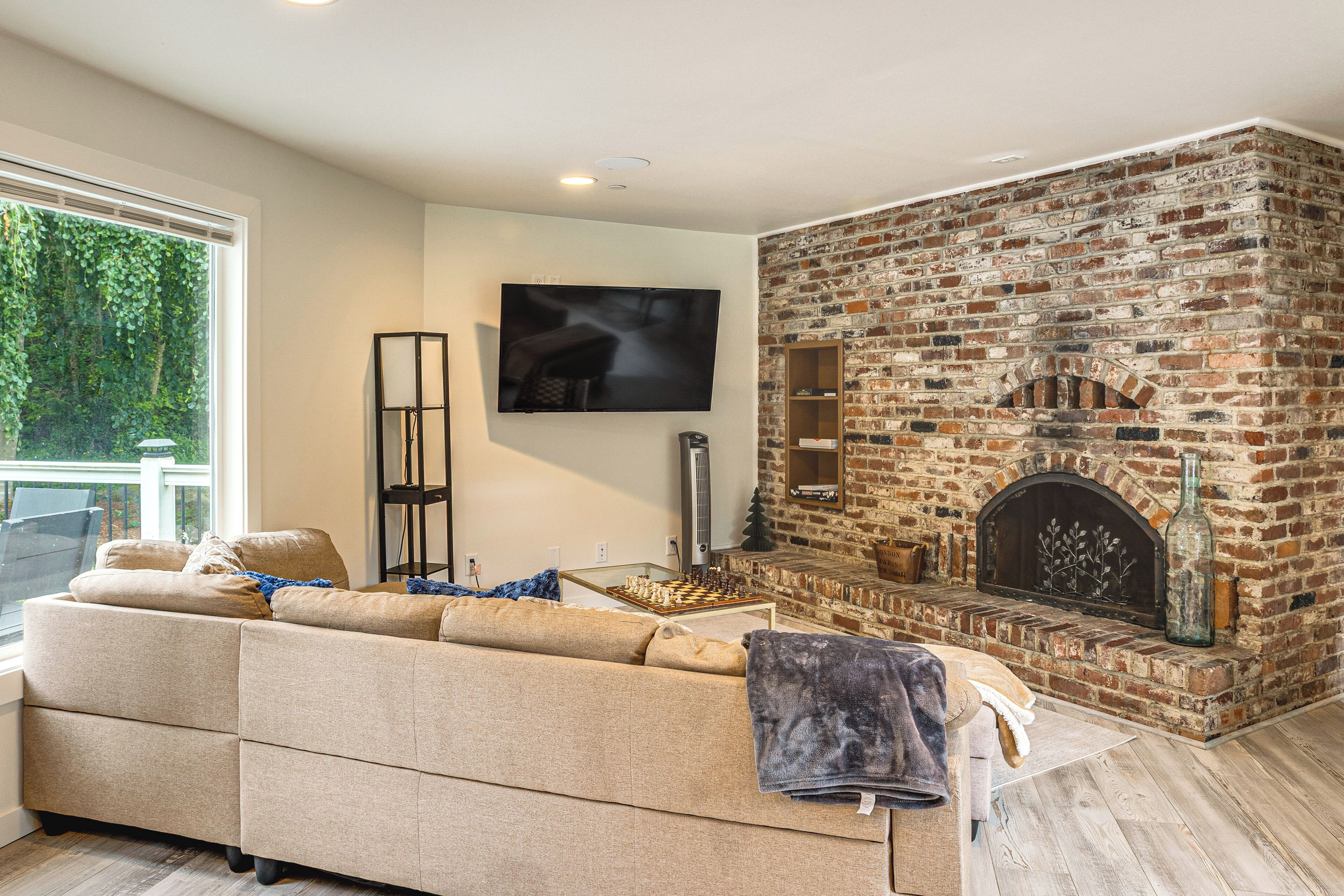 Una sala de estar con chimenea de ladrillo, un sofá color beige, un televisor de pantalla plana y un ventanal grande.