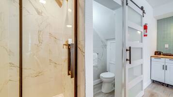 A modern bathroom with a glass shower enclosure, a toilet, and a sink area with cabinets.