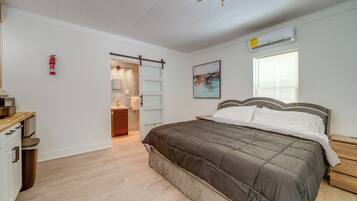 A bedroom with a bed, a nightstand, a wooden dresser, a fire extinguisher, and a sliding door leading to a bathroom.