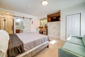 A modern bedroom with a bed, a green sofa, a bathroom with a shower, and a small kitchenette. - Walkable Location! High-end 4-unit Hinton Getaway (Hinton)