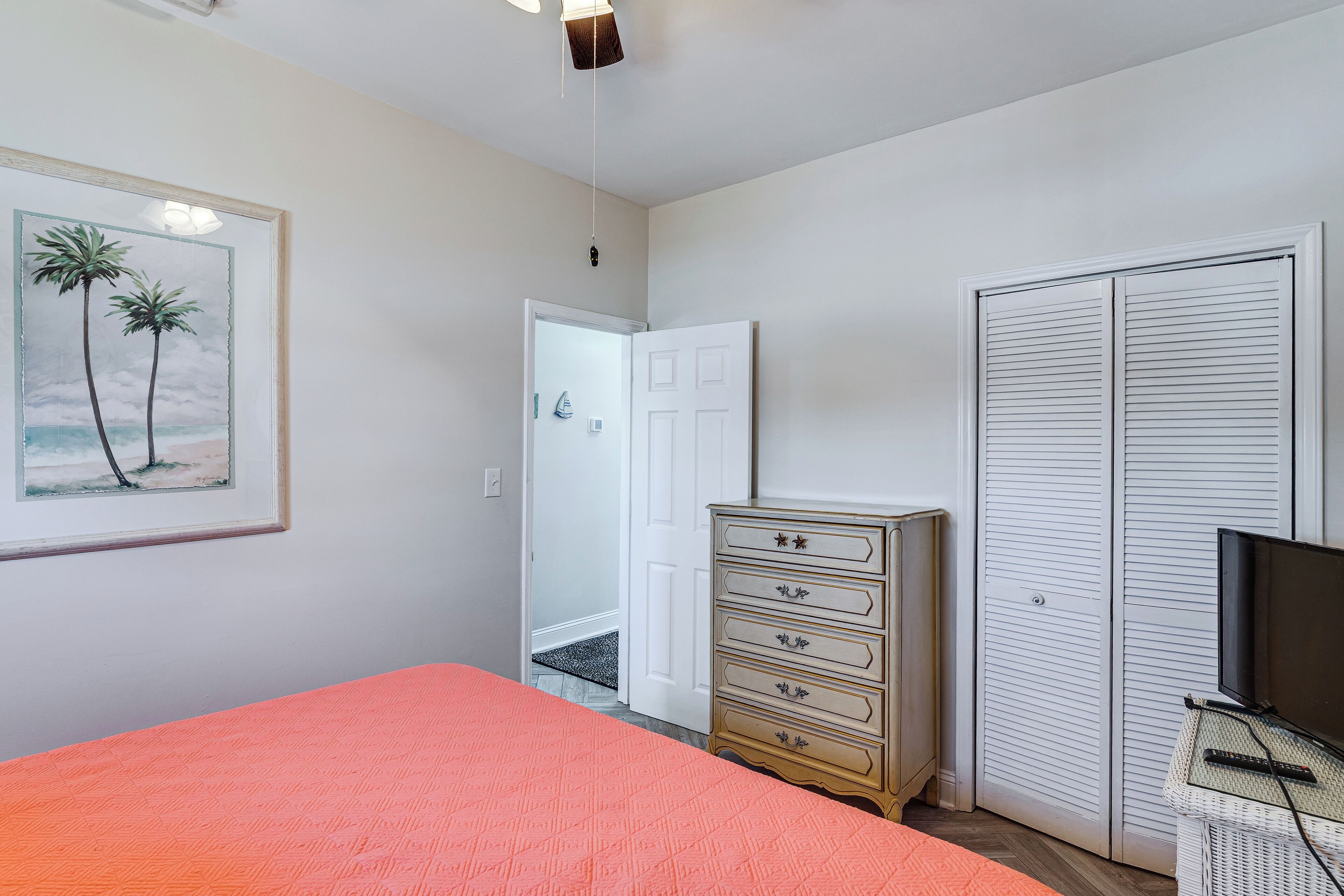 A bedroom with a bed, a dresser, a television, a door, and a framed picture on the wall.