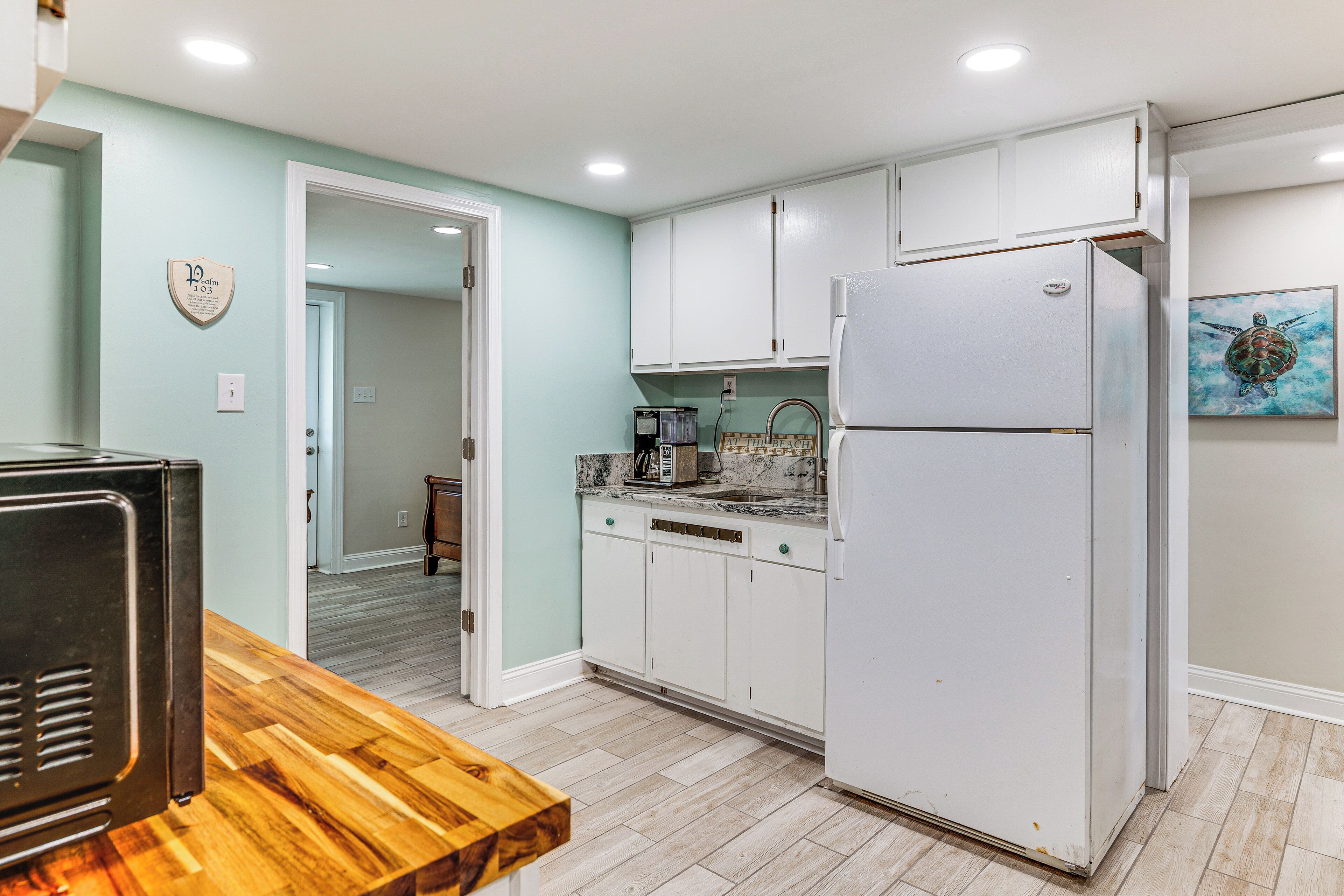 A kitchen with white cabinets, a refrigerator, a wooden table, and a painting on the wall.