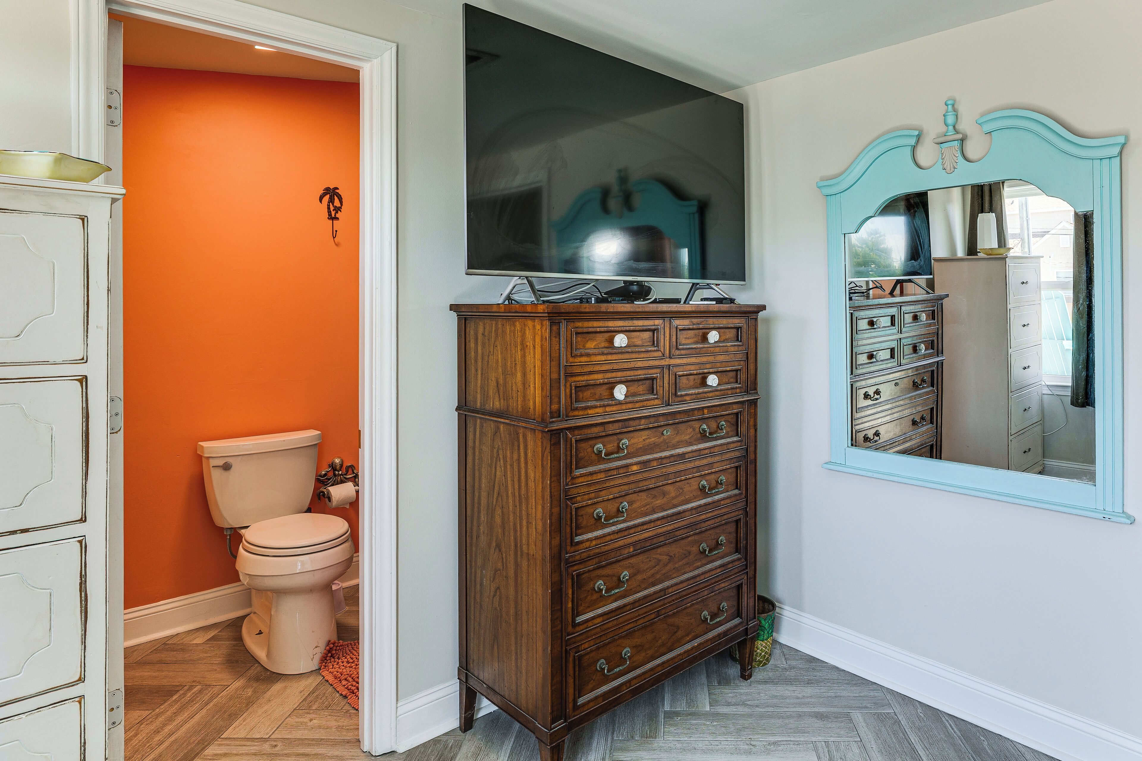 Un baño con inodoro, cómoda de madera y un espejo grande.