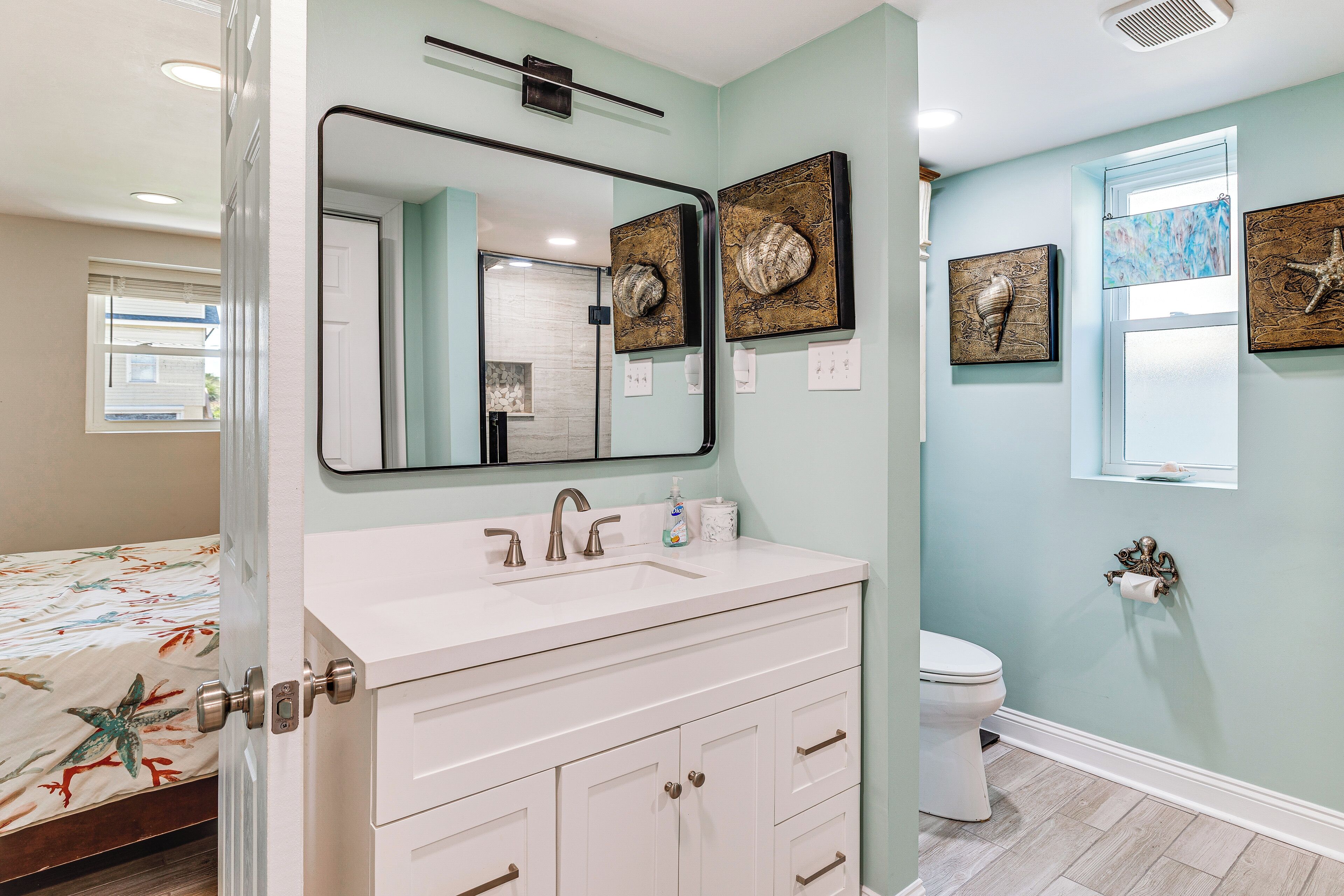 A bathroom with a white vanity, a mirror, a toilet, and artwork on the walls.