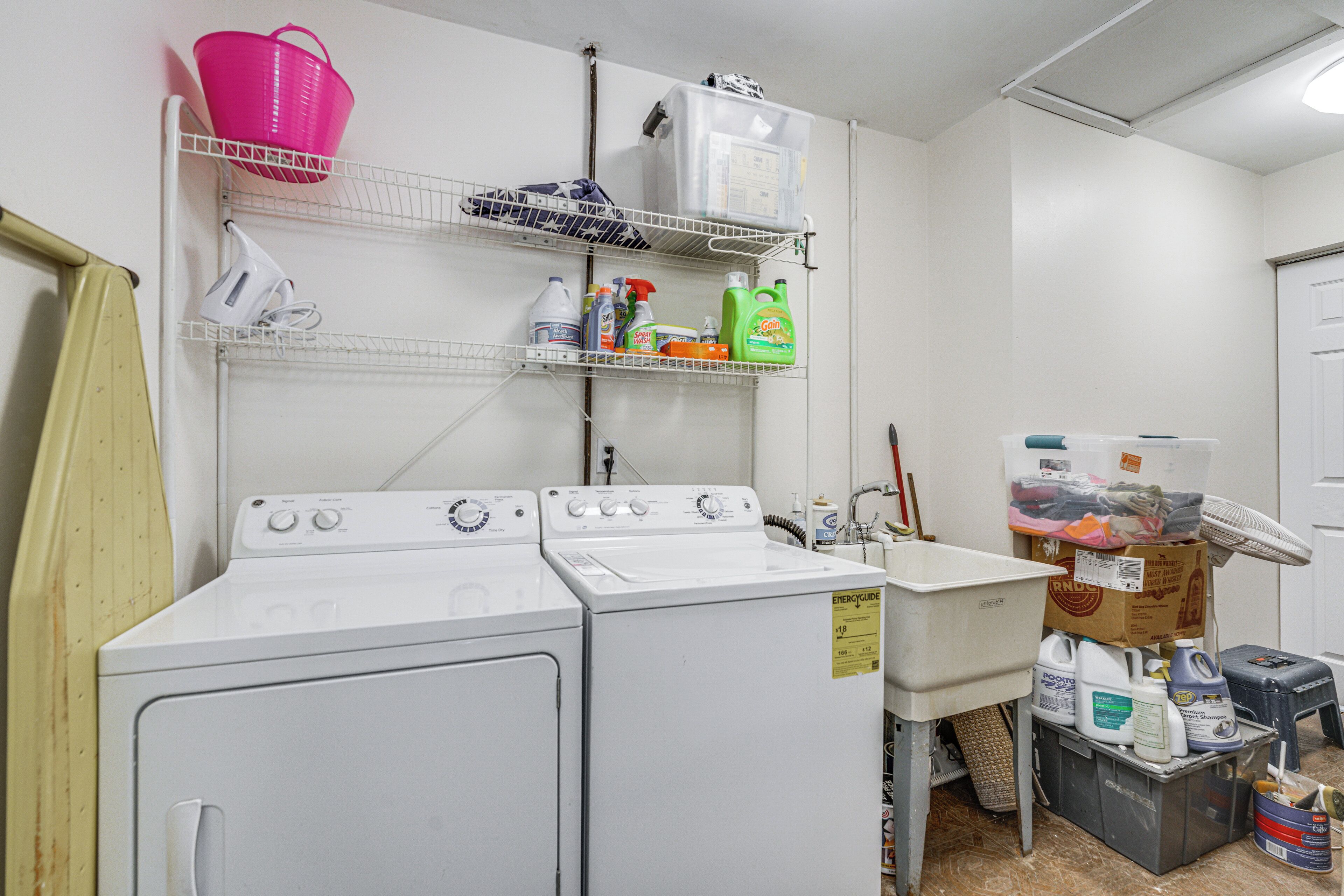 A laundry room with two washing machines, shelves with cleaning supplies, and a sink.